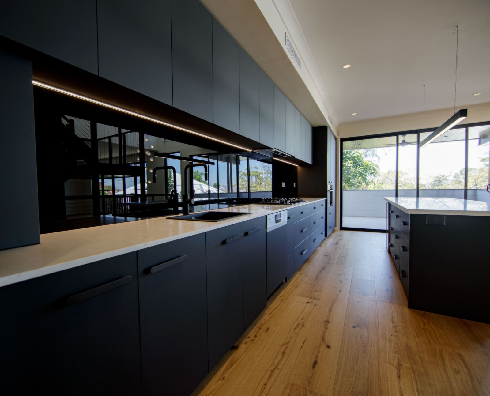 Long kitchen in dark joinery with timber floors